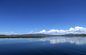 An aerial view of the blue waters of Blackfoot Reservoir with mountains in the far distance on a cloudless blue day near Soda Creek Campground in Soda Springs, Idaho.